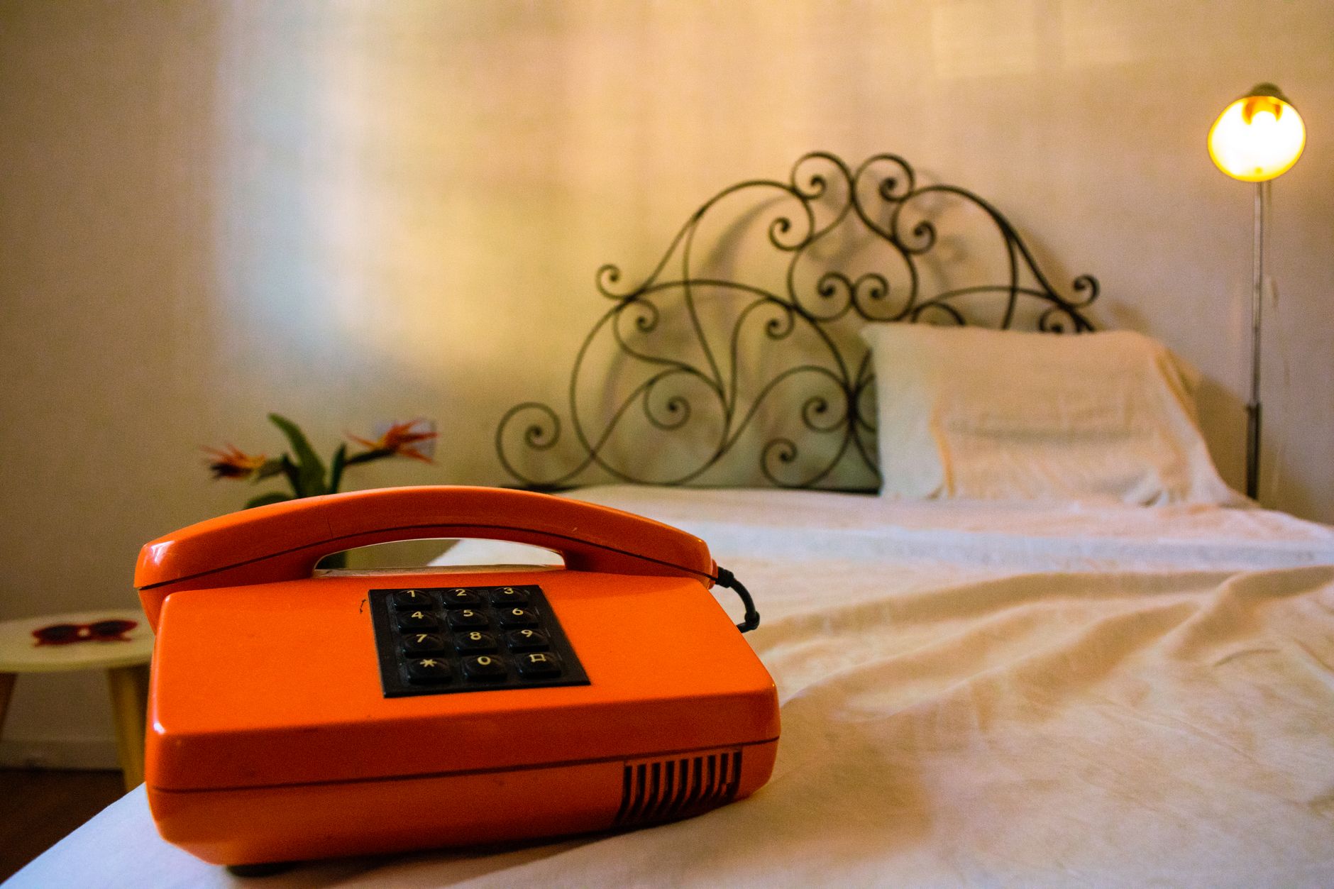 Vintage orange phone beside an empty bed, creating a quiet scene of waiting for contact.