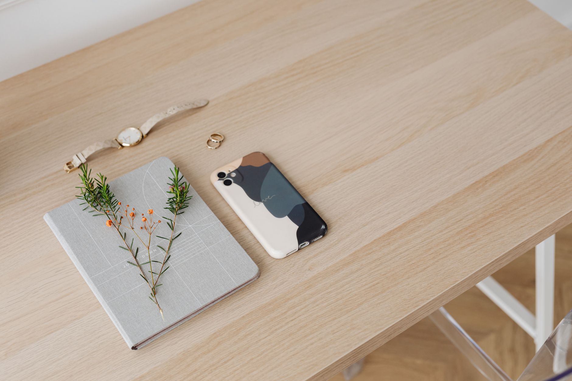 A phone beside a gray notebook and small plant stems on a light wooden table