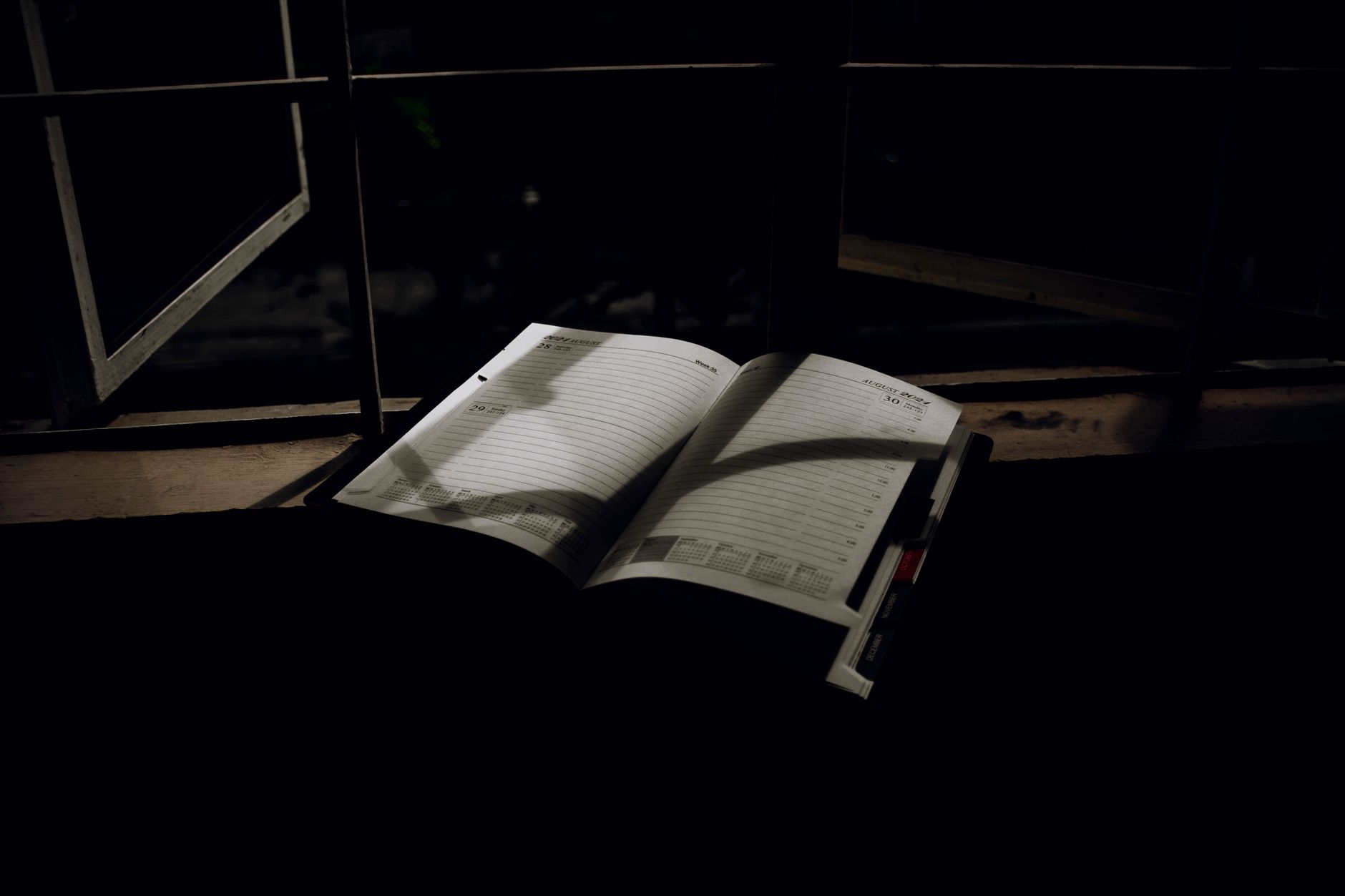 An open planner with dramatic lighting sits on a window sill at night.