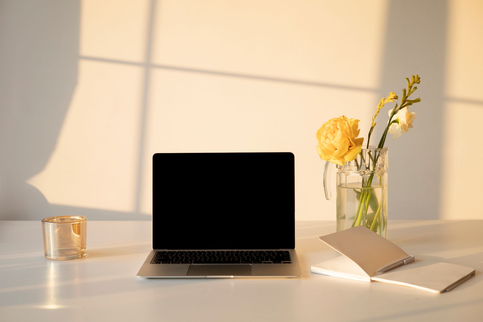 A serene minimalist workspace with a laptop, flowers, and a notebook in soft morning light